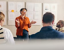 A business professional stands and speaks to a group of colleagues.